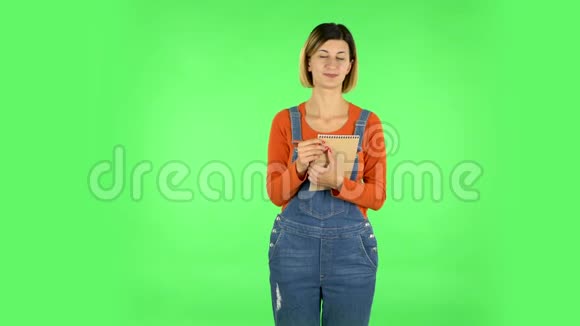 女孩站着思考然后快乐地用铅笔在笔记本上写字绿色屏幕视频的预览图