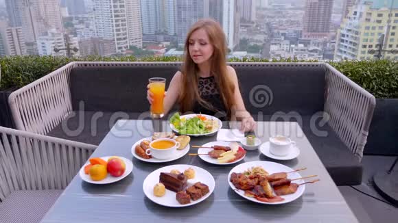 美丽的女孩独自坐着在屋顶城市酒吧用餐喝橙汁视频的预览图