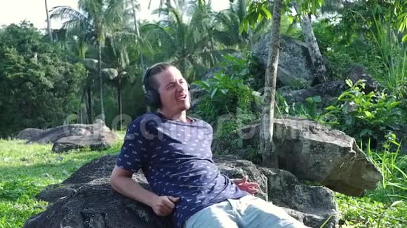 一个男人坐在岩石上一边听音乐一边戴着耳机视频的预览图
