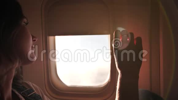 一个年轻的女孩打开飞机的窗帘享受飞行视频的预览图