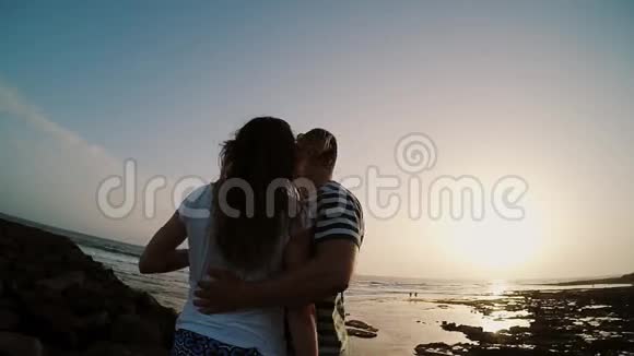 男人和女人站在海边拥抱和看日落晚上海滩上的情侣动作缓慢视频的预览图