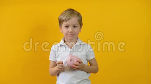 小男孩把硬币放在黄色背景上的储蓄罐里视频的预览图