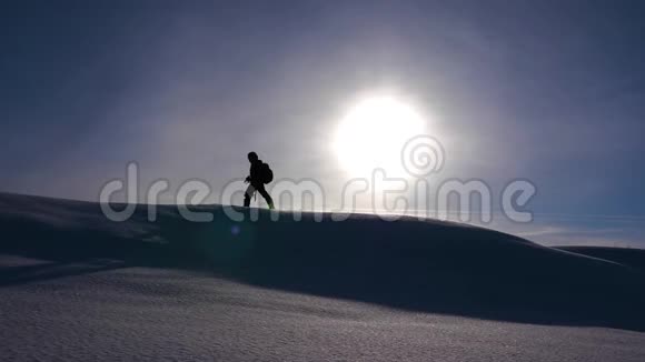 旅行者在阳光下在雪山上行走冬天的摄影师旅行者穿着黄色的光芒登上雪岭视频的预览图