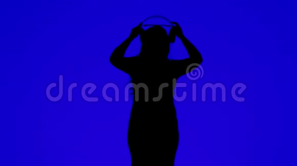 一位身材苗条的女士戴着耳机在蓝色背景下随着音乐起舞的剪影视频的预览图