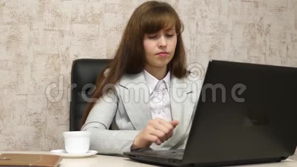 漂亮的女孩坐在办公室的椅子上在笔记本电脑上打字喝着白色杯子里的咖啡年轻女子视频的预览图