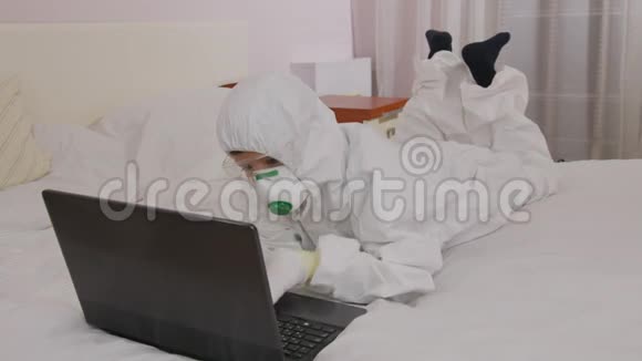 一个穿着防护服和呼吸器的男孩在家里的电脑上被隔离在流行病期间视频的预览图