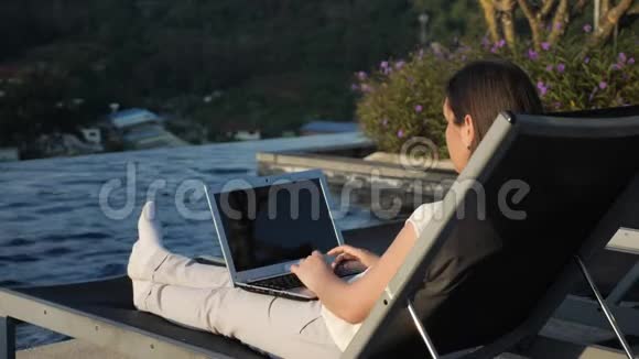 女孩的笔记本电脑休息在酒店游泳池对布什视频的预览图