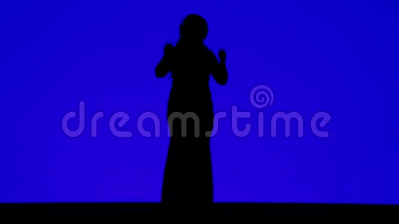 一个戴着耳机的苗条女人在蓝色背景下随着音乐起舞的剪影视频的预览图