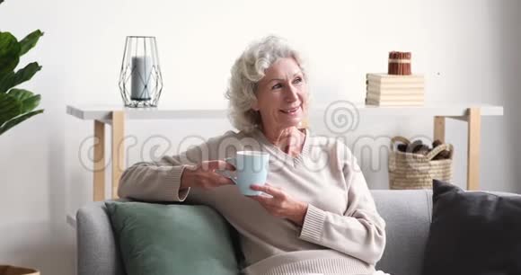 微笑的老太太喝着茶看着家里的摄像机视频的预览图