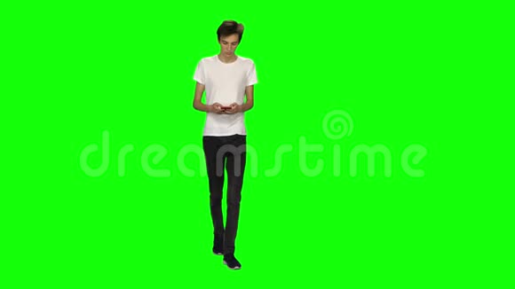 高个子瘦小的年轻人平静地走着在绿色屏幕上发短信给他的手机铬钥匙前景视频的预览图