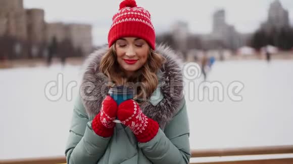 美丽可爱的中年女孩卷发温暖的冬季夹克站在冰场背景镇广场视频的预览图