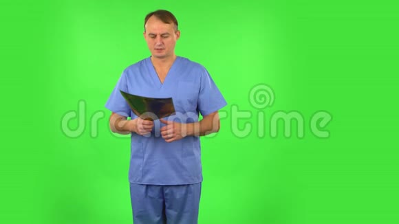 男医生穿着蓝色外套用x光检查快照并解释绿色屏幕视频的预览图