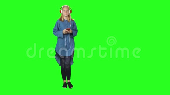 少女从容地走在大红耳机里在绿色屏幕上的手机上选择音乐前景视频的预览图