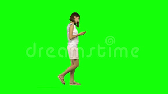 年轻女子平静地走着在绿色屏幕上给她的手机发短信侧写视图视频的预览图