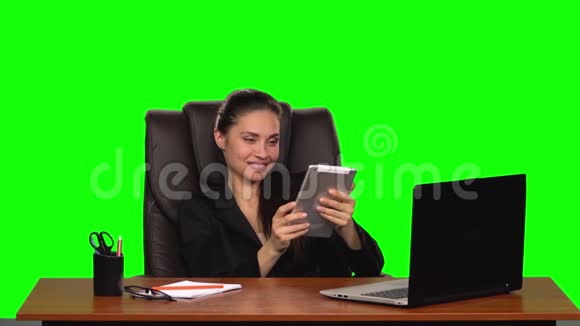 工人女孩坐在一个工作场所靠在一张皮椅上在平板电脑上交流风趣的微笑绿色视频的预览图