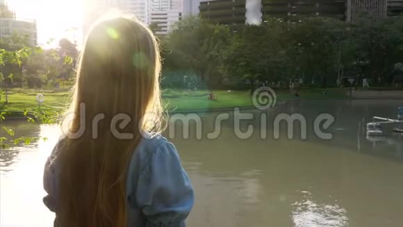 美丽的快乐女孩站在公园的湖边夕阳下的树木视频的预览图