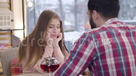 一张无聊的白种美女用智能手机和男朋友或丈夫坐在餐厅里做配偶的照片视频的预览图