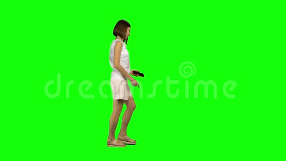 棕色光滑头发的年轻女子平静地在绿色屏幕上的手机上行走和交谈侧写视图视频的预览图