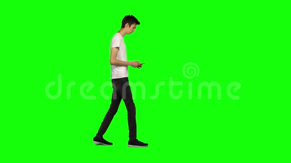 高个子瘦小的年轻人平静地走着在绿色屏幕上发短信给他的手机铬钥匙侧写视图视频的预览图