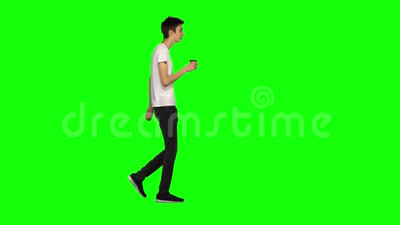 高大瘦小的年轻人平静地走着在绿色的屏幕背景下喝着咖啡铬钥匙4k射击侧写视图视频的预览图