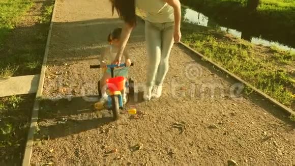 快乐的女儿骑自行车小孩子学会骑自行车由他的母亲妈妈教女儿骑自行车视频的预览图