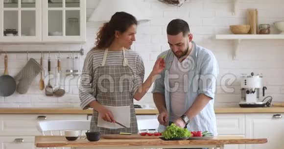 快乐迷人的女人在一起做饭的时候喂丈夫视频的预览图