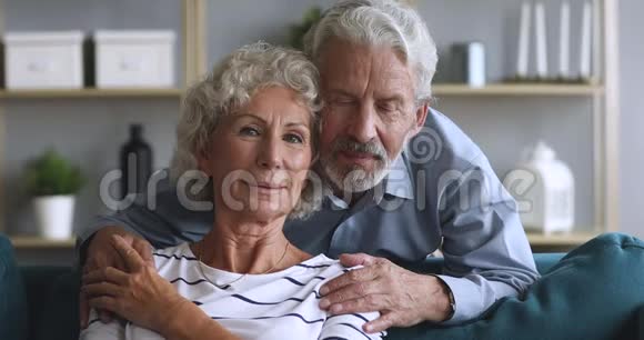 可爱的老丈夫拥抱坐在沙发上微笑的老女人视频的预览图
