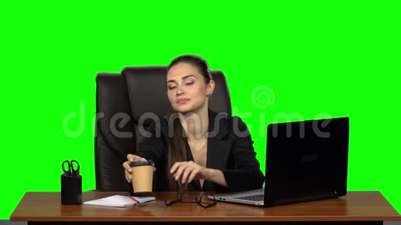 商务女性坐在办公桌前的皮革椅子上喝咖啡绿色屏幕工作室慢动作视频的预览图