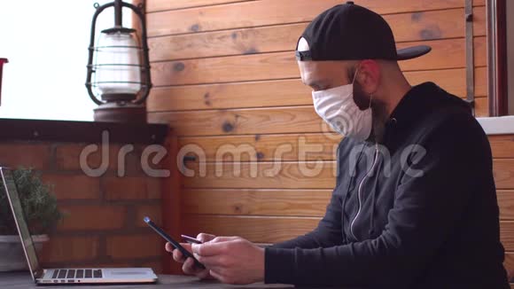 戴防护医疗面罩和黑色帽衫的商人用信用卡和智能手机在线支付费用视频的预览图