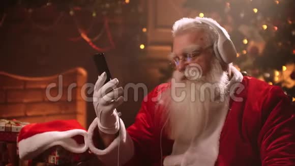 圣诞老人坐在椅子上通过耳机电话和舞蹈听音乐视频的预览图
