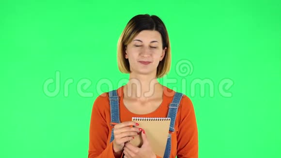 女孩站着思考然后快乐地用铅笔在笔记本上写字绿色屏幕视频的预览图