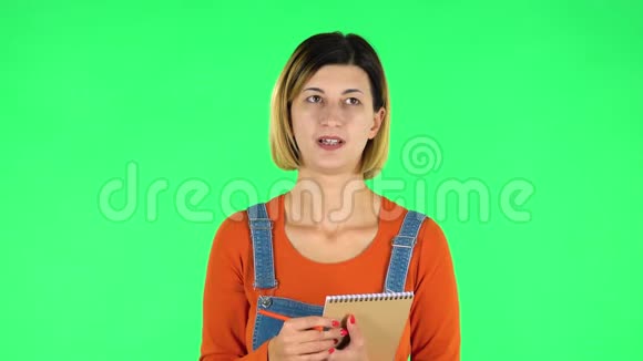 女孩站着思考然后专心地用铅笔在笔记本上写绿色屏幕视频的预览图