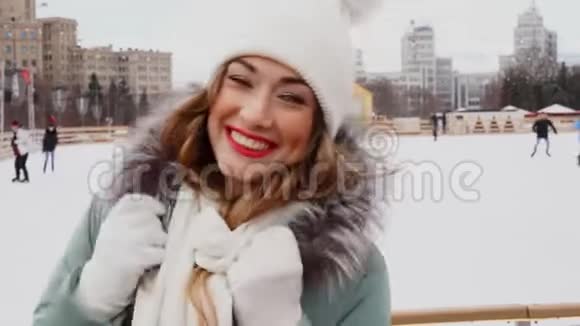 美丽可爱的中年女孩卷发温暖的冬季夹克站在冰场背景镇广场视频的预览图