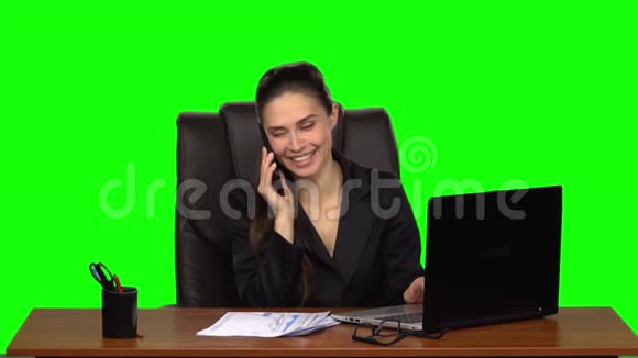 女人在笔记本电脑上工作在电话上愉快地说话绿色屏幕慢动作视频的预览图