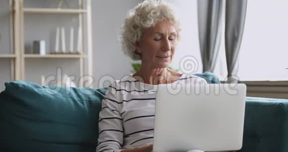 快乐的老奶奶用电脑独自坐在客厅里视频的预览图