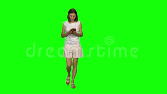 棕色光滑头发的年轻女子平静地在绿色屏幕上的手机上行走和交谈前景视频的预览图