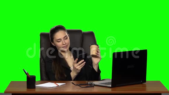 商务女性坐在皮椅的办公桌前用手机写信息喝咖啡绿色屏幕工作室视频的预览图