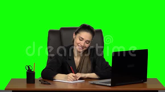 漂亮的女孩带着幸福的微笑在笔记本上写字绿色屏幕工作室慢动作视频的预览图