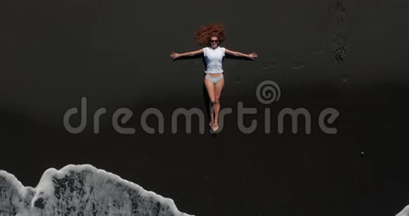 空中观景美丽的女人躺在特内里费的黑色海滩上休息而一个漫长的海洋浪潮即将到来视频的预览图