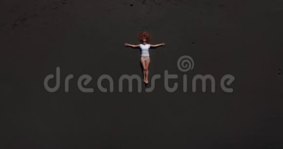 空中观景美丽的女人躺在特内里费的黑色海滩上休息而一个漫长的海洋浪潮即将到来视频的预览图