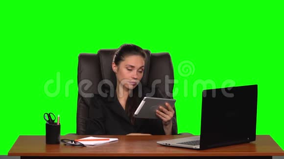 女工坐在一个工作场所靠在一张皮椅上在平板电脑上交流心烦意乱绿色屏幕视频的预览图