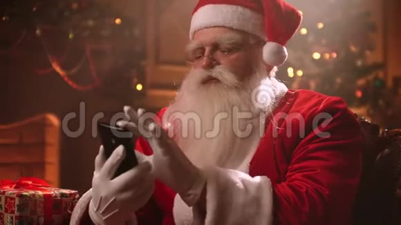 圣诞老人使用智能手机和他的助手聊天并监控世界局势视频的预览图