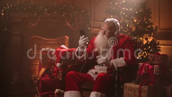 圣诞前夜一位留着白胡子的老人穿着圣诞老人服装听音乐新的圣诞老人视频的预览图