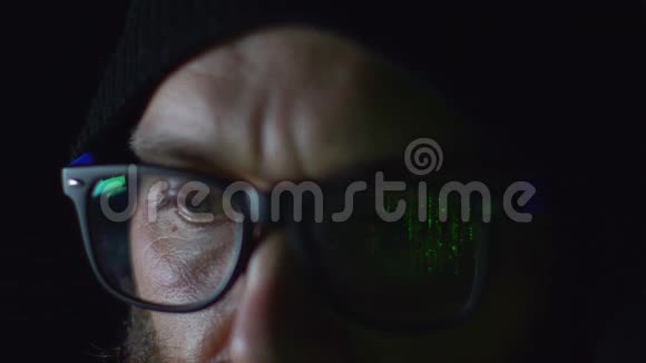戴眼镜的胡子黑客在电脑上工作在夜间绿色编程代码中反射眼镜关闭4k镜头视频的预览图