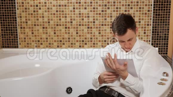穿着裤子和衬衫的人正躺在浴室里学习文件视频的预览图