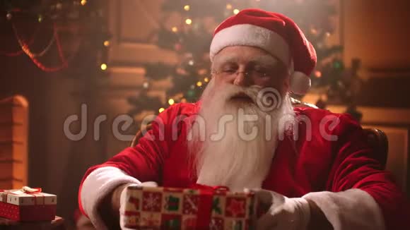 一位留着白胡子穿着圣诞老人服装的老人把礼物递给相机微笑着视频的预览图