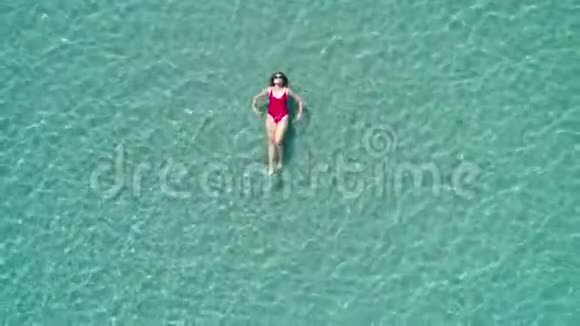 在晶莹剔透的绿松石海洋中年轻漂亮性感的女孩穿着红色泳衣漂浮在水面上快乐视频的预览图