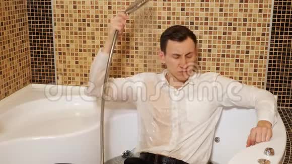 穿着衬衫和裤子的人躺在淋浴下的浴缸里视频的预览图