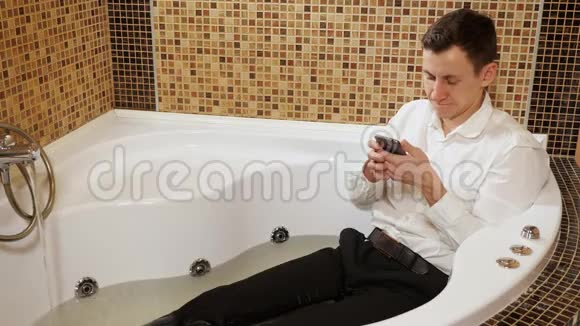 穿着裤子穿着带电话的衬衫的人正躺在一个水浴中视频的预览图