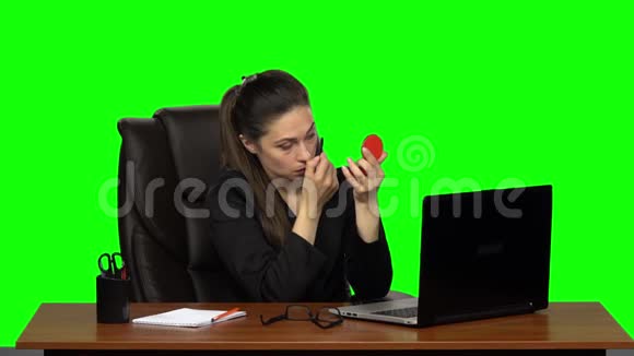 女人坐在皮椅上的桌子上在睫毛上涂上睫毛膏看着绿色屏幕上的红色镜子慢慢视频的预览图